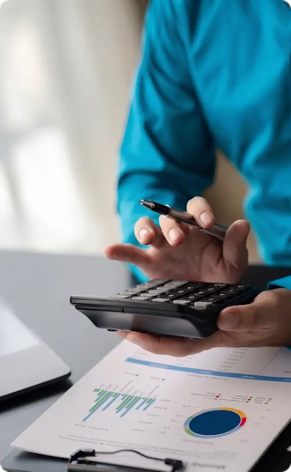 Financial specialist in a blue shirt using a calculator to review business loan charts and funding data.
